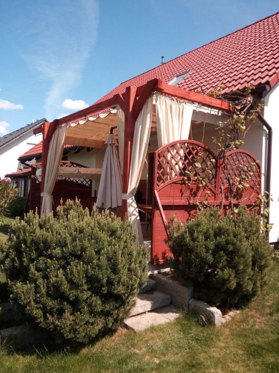 Custom waterproof outdoor curtains hanging on a wooden garden pergola with decorative privacy screens.