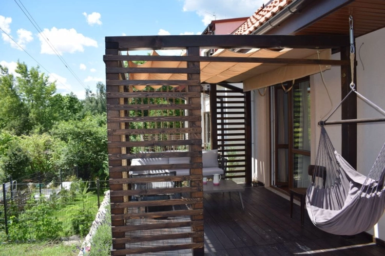 Premium waterproof retractable Roman shade mounted on a wooden pergola over a cozy outdoor terrace with furniture.