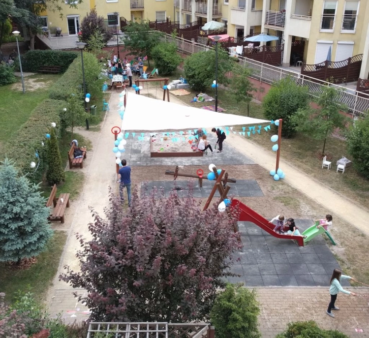 White triangular sun shade sail 5x5x7m installed over a children's playground area with a sandbox and slides