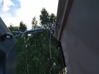 A turnbuckle and wire cable attaching a waterproof terrace Roman blind to a mounting bracket on a dark grey pole