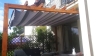 Grey and white striped retractable Roman shade canopy on a wooden pergola over a patio with garden furniture.