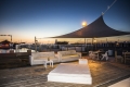 Lightweight triangular sun shade sail installed over an outdoor wooden deck with lounge furniture at sunset