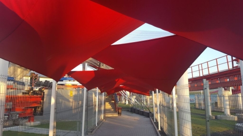 Red triangular waterproof sun sail shades installed over a walkway in an outdoor recreational area