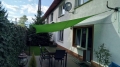 Grünes Sonnensegel wasserdicht 2x2 m montiert über einer Terrasse mit Gartenmöbeln bei einem Einfamilienhaus