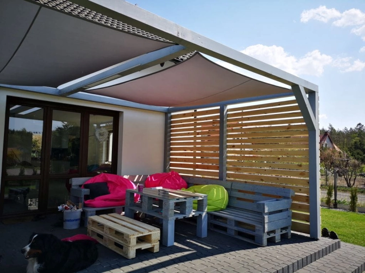 Vela ombreggiante impermeabile 4x4m montata su un pergolato in legno sopra un terrazzo con mobili in pallet