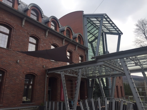 Brown triangular waterproof sun sail shade installed on a brick building exterior with a modern metal structure.