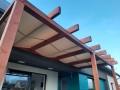Toldo de pérgola premium impermeable montado bajo vigas de madera de terraza como protección solar