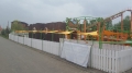 Gelbes dreieckiges Sonnensegel über einem Weg in einem Freizeitpark neben einer Achterbahn