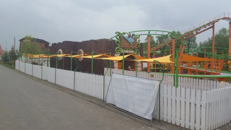 Yellow triangular waterproof sun shade sails installed above a waiting area near a green and orange roller coaster.