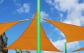 Orangefarbenes dreieckiges Sonnensegel Premium für den Garten an einem hohen grünen Mast montiert