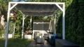 White sliding retractable waterproof sun shade sail mounted on a wooden garden pergola with outdoor lounge furniture.