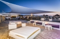 Large triangular sun shade sail over an outdoor lounge area with white patio furniture and sofas.