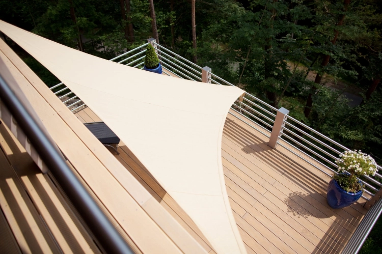 Dreieckiges Sonnensegel auf einer Terrasse mit Holzboden und Geländer am Waldrand