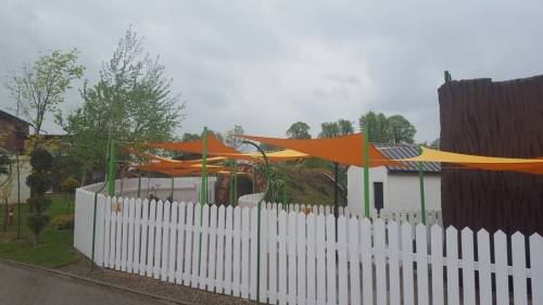 Large orange triangular waterproof sun shade sails installed with green poles over a fenced outdoor playground area