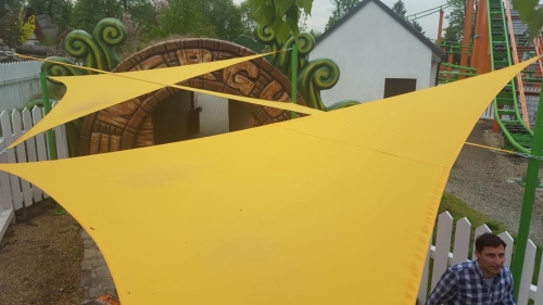 Yellow triangular waterproof shade sail installed in an outdoor playground area for sun protection.