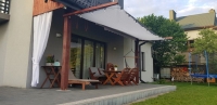Custom-sized white retractable sun sail shade installed over a modern house patio with outdoor furniture and lighting.