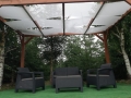 White sun shade fabric strips woven through a wooden pergola roof over a black wicker patio furniture set.