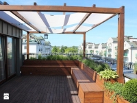 Custom-size white shade sail strip installed on a wooden rooftop pergola with garden benches and planters