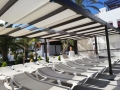 Toldos romanos blancos instalados en una pérgola oscura sobre tumbonas en el jardín de un hotel