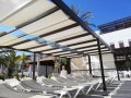 Tenda a pacchetto romana bianca montata su una struttura scura sopra i lettini a bordo piscina