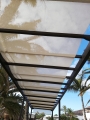 Tenda romana bianca montata su un pergolato marrone circondato da palme su sfondo cielo blu