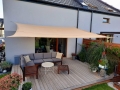 Beige rechthoekig schaduwdoek 4x6 m van HDPE gemonteerd boven een terras met tuinmeubelen en planten