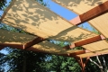 Beigefärgad solskyddsväv av HDPE monterad på en träpergola i trädgården