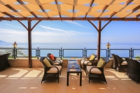 Woven HDPE sunshade sail fabric installed on a wooden pergola over an outdoor patio with sea views.