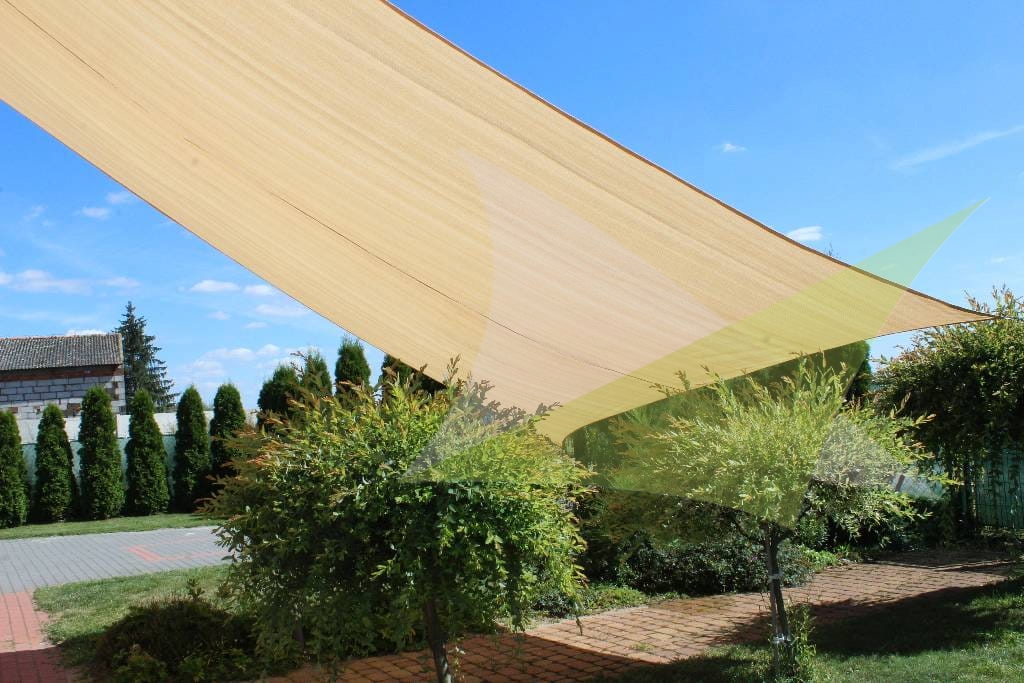 Large sand-colored square HDPE sun shade sail over a garden patio with green trees and a blue sky background