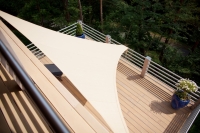 Vela ombreggiante triangolare premium 5,2x5,2x5,2 m in beige montata sopra una terrazza con vista sul bosco