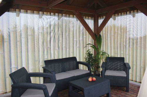 Outdoor gazebo screen with bamboo print and black wicker garden furniture set consisting of a sofa, chairs, and table
