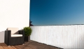 Witte balkonafscheiding op maat met houtprint, gemonteerd op de terrasleuning met loungemeubel
