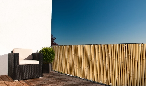 Natural bamboo-look privacy screen for a balcony fence with matching outdoor chair and plant on a sunny deck
