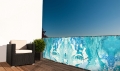 Balkonscherm op maat met blauwe abstracte graphics gemonteerd op de terrasleuning bij een fauteuil