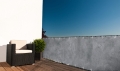 Grijs balkonscherm met betonlook, gemonteerd op terrashekwerk met fauteuil en plant in pot