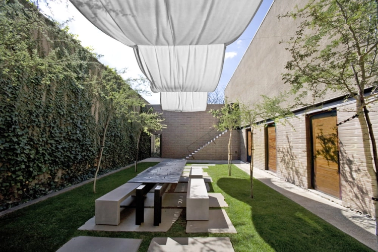 White waterproof рим roman shade canvas fabric hanging over a modern outdoor patio with long table and ivy wall