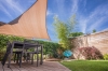 Triangular sand HDPE sun sail over a wooden garden deck with table and chairs on a sunny day.