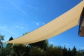 Beige rechthoekig schaduwdoek HDPE 3x4 m gemonteerd in de tuin tegen een blauwe lucht