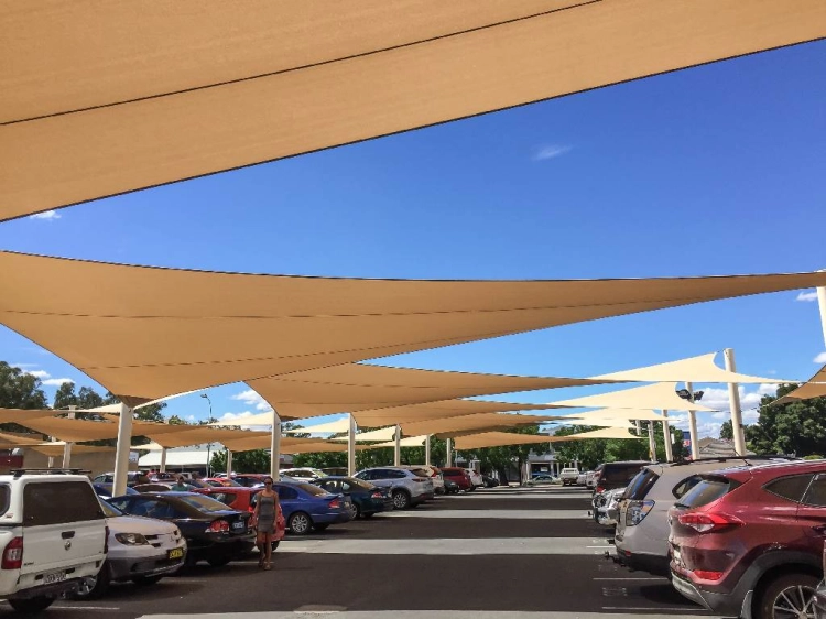 Custom-sized waterproof PVC sun shade sails providing shade for a car parking lot on a sunny day.