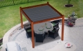Grey waterproof Roman blind for a wooden pergola with a patio table and chairs set on a paved backyard terrace