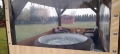 Clear custom-fitted patio enclosure tarp protecting an outdoor hot tub and seating area from wind and rain