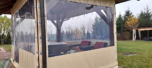 Custom clear patio side panel tarp with beige border installed on a wooden gazebo enclosing a hot tub and outdoor furniture