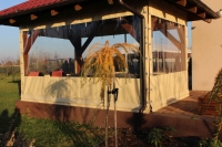 Custom clear PVC terrace cover with tan vinyl borders installed on a wooden garden gazebo in a sunny lawn setting