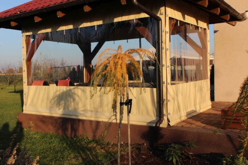 Custom clear PVC terrace cover with tan vinyl borders installed on a wooden garden gazebo in a sunny lawn setting