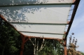 Maßgefertigtes weißes Sonnensegel an einer Holzpergola im Garten montiert.