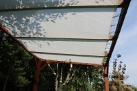 Vela ombreggiante bianca su misura montata su una pergola in legno in giardino.