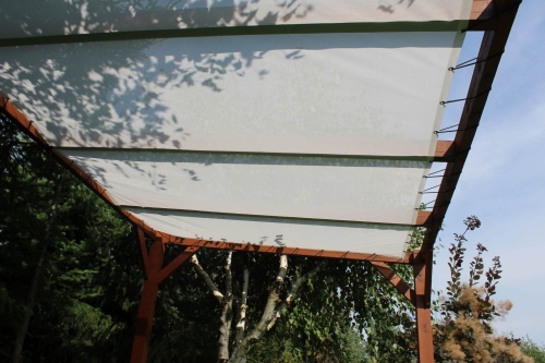 White custom retractable garden sun shade sail canopy on a wooden pergola structure in a backyard setting