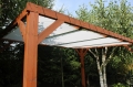 Weißes Sonnensegel nach Maß montiert unter einer Holzkonstruktion der Pergola im Garten