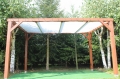 Weißes Sonnensegel nach Maß montiert auf einer Holzpergola im Garten