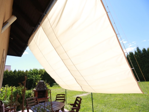 Premium waterproof retractable beige sun sail shade over a patio with outdoor furniture and a lush green lawn.